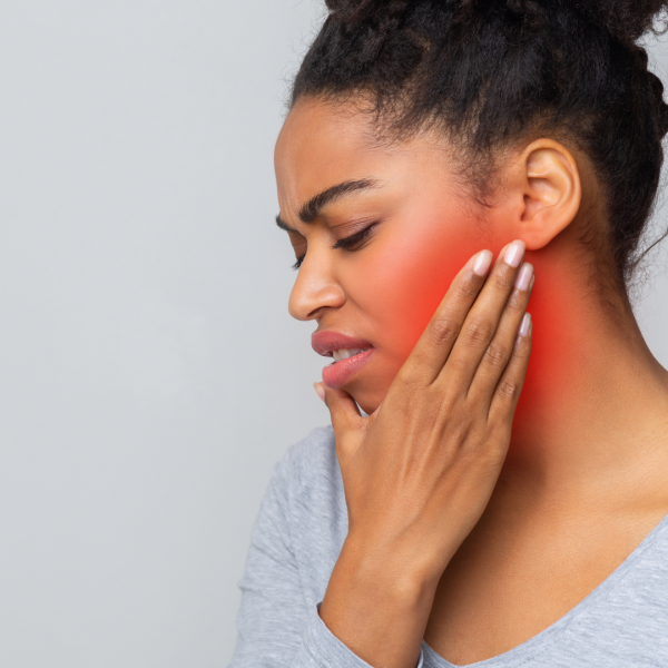 a woman winces while rubbing her left jaw with her hand, trying to alleviate the pain from teeth grinding that can be caused by psychiatric medication and stress and treated by Dr. Rachel Dillinger